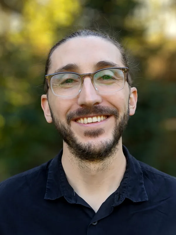 Jake W. Vincent smiling outdoors in front of green foliage.